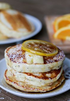 lemon ricotta poppy seed pancakes on a white plate with orange slices and powdered sugar