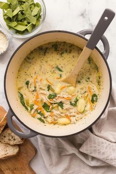 a pot filled with soup next to bread and salad