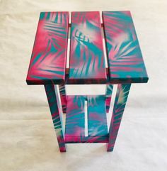 a small table made out of wood and painted pink, blue and green with palm leaves on it