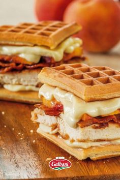 two waffle sandwiches sitting on top of a wooden cutting board next to peaches