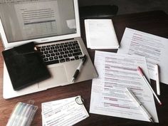 an open laptop computer sitting on top of a wooden desk next to papers and pens