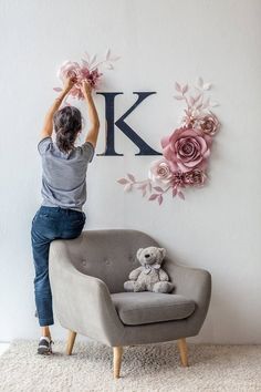 a person sitting on a chair with a teddy bear in front of the letter k