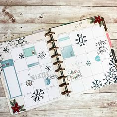 an open planner with snowflakes and christmas decorations on the pages is sitting on a wooden surface