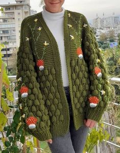 a woman wearing a green knitted cardigan with flowers and mushrooms on it