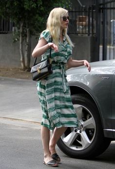 a woman in a green and white striped dress is walking past a car on the street