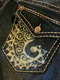 the back pocket of a pair of jeans with an ornate design on it and a gold button