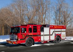 a red fire truck is parked on the side of the road near some trees and snow