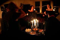 a group of people standing around a table with food and candles in the middle of it