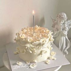 a white cake with a candle on it and an angel figurine next to it