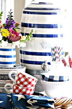 blue and white striped vases with flowers in them sitting on a table next to plates