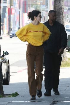 a woman wearing a yellow sweater and brown pants is walking down the street with a man