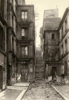 an old black and white photo of a narrow street with stairs leading up to buildings