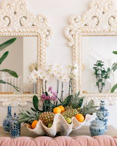 a table topped with vases filled with fruit and flowers next to two framed mirrors