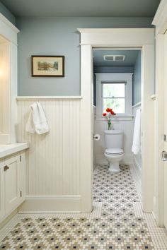 a white toilet sitting in a bathroom next to a sink under a window on top of a tiled floor