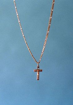 a cross is hanging from a gold chain on a blue sky background with a plane in the distance