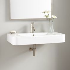 a white sink sitting under a bathroom mirror next to a vase with flowers in it