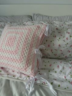 a pink and white crocheted pillow on top of a bed next to pillows