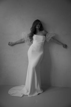 a woman in a white dress leaning against a wall with her arms stretched out to the side