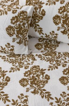 a bed with white and gold floral print on the comforter, two pillow cases are next to each other