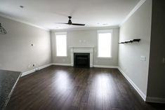 an empty living room with hard wood flooring and a fire place in the corner