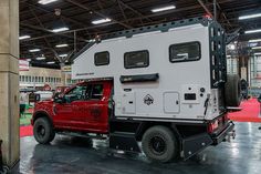 a red truck is parked in a large warehouse with other trucks and people around it