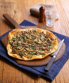 a pizza sitting on top of a wooden cutting board next to a knife and fork