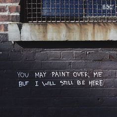 graffiti written on the side of a brick wall near a window with bars in it