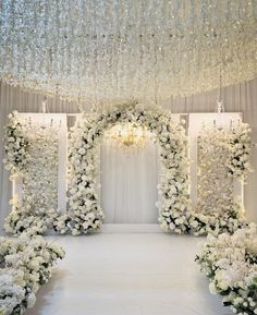 an aisle decorated with white flowers and chandelier hanging from the ceiling above it