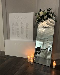 candles are lit in front of a large mirror with a seating chart on the wall