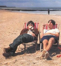 two men sitting in lawn chairs on the beach