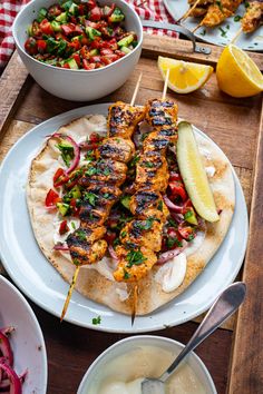 chicken skewers are served on pita bread with salad and lemon wedges