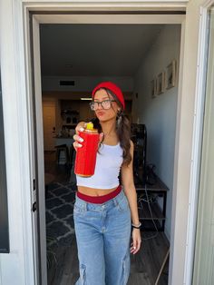 a woman holding a red drink in her right hand and wearing a red beanie