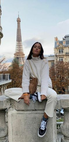 a woman sitting on top of a stone wall next to a tall building with the eiffel tower in the background