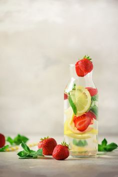 two glass bottles filled with lemon, strawberries and lime slices next to each other