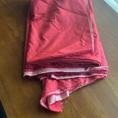 three pieces of red cloth folded on top of a wooden table next to a window