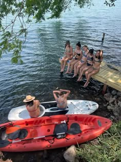 several women are sitting in kayaks at the edge of a body of water, with one woman standing up