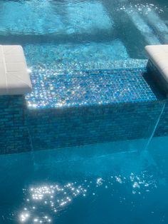 an empty swimming pool with sun reflecting off the water and blue tiles on the side