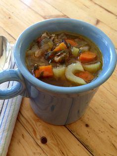 a blue bowl filled with soup on top of a wooden table next to a spoon