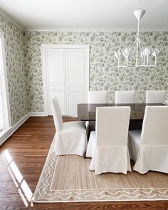 a dining room table with white chairs and a rug on the floor in front of it