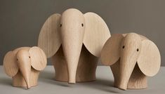 three wooden elephants standing next to each other in front of a gray wall and floor