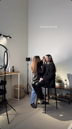 two women are sitting in chairs and one is getting her hair styled by another woman