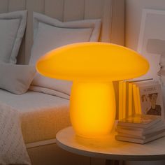 a yellow mushroom lamp sitting on top of a table next to a white bed and pillows