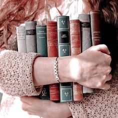 a woman is holding a stack of books in her hands and wearing bracelets on her wrist