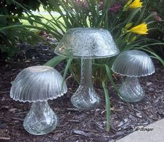 three glass mushrooms sitting on the ground next to flowers