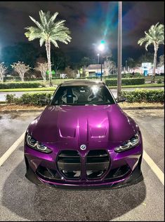 a purple sports car parked in a parking lot at night with palm trees behind it