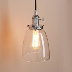 a clear glass light fixture hanging from the ceiling in a room with a beige wall behind it