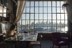 a woman sitting at a table in front of a window looking out on the city