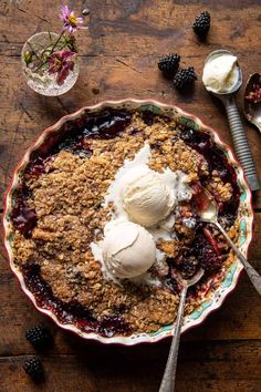 a bowl filled with fruit and ice cream next to two spoons on top of a wooden table