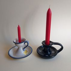 two tea cups and saucers with red candles in them on a white table top