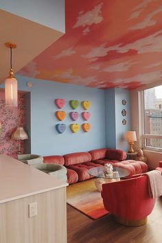 a living room filled with lots of furniture and walls covered in colorful clouds painted on the ceiling